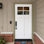 A fresh Craftsman entry with a bright white door, four-pane glass, black hardware, and soft sage trim—finished by Paintmasters.